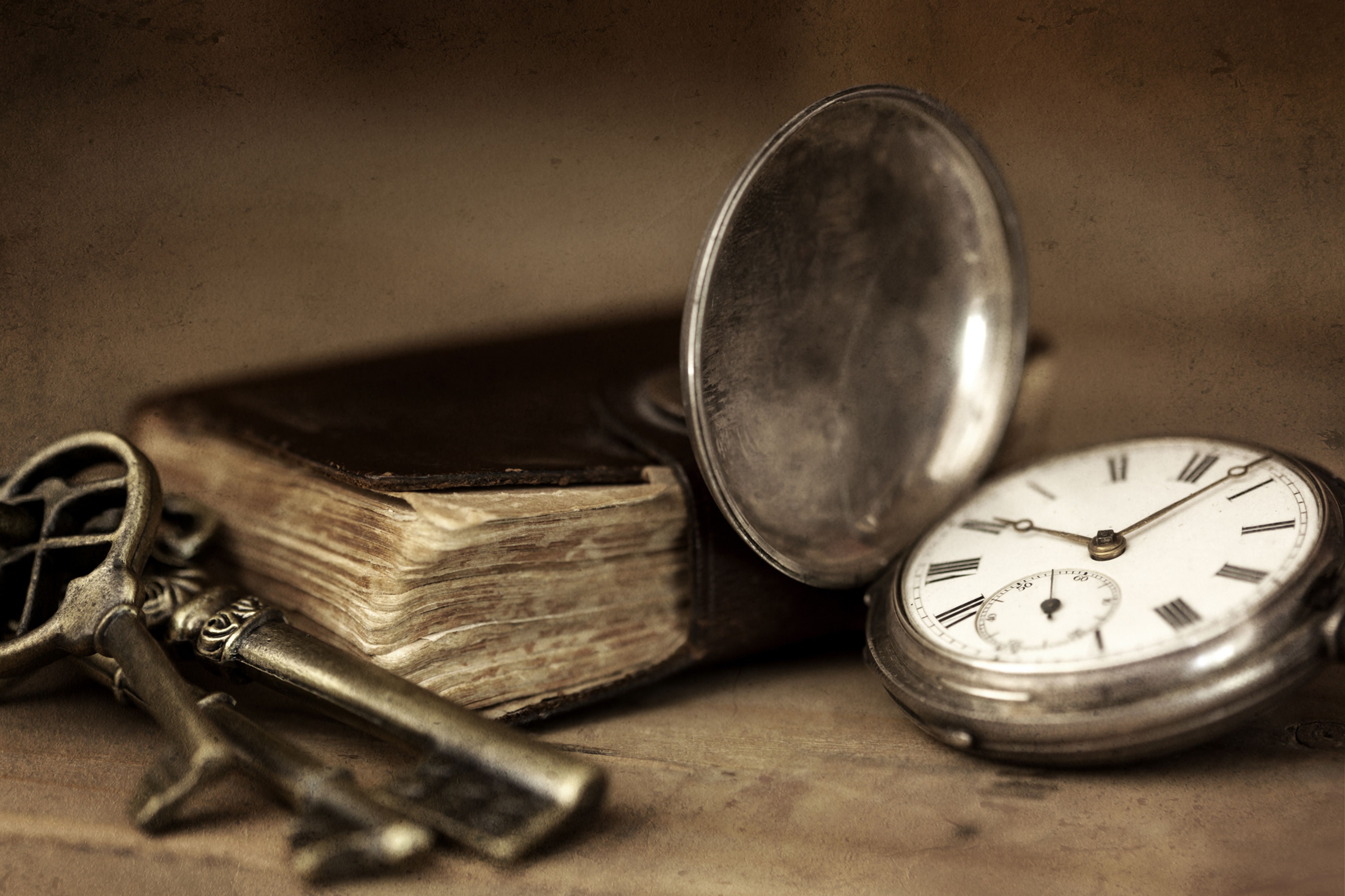 Silberne Taschenuhr neben einem alten Buch und Messingschlüsseln